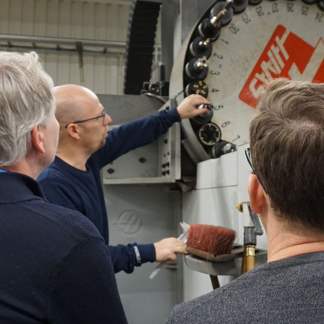 Group of people observing a machine operator changing tools on a CNC milling machine.
